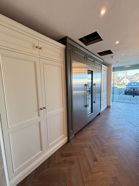 A wall of floor to celing white cupboards on either side of a full size fridge in the DeBarra Kitchen showroom after being hand painted by Impressions painting and decorating