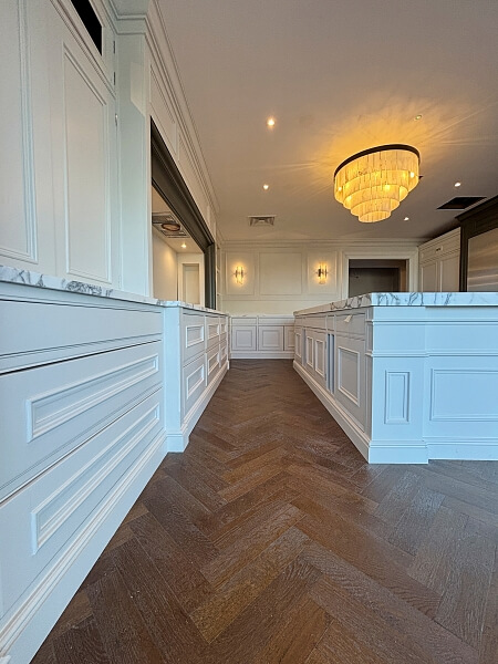 A white kitchen island with drawers and a white marble top on a right and a wall on the left with white drawers and cabinets in the DeBarra Kitchen showroom after being hand painted by Impressions painting and decorating