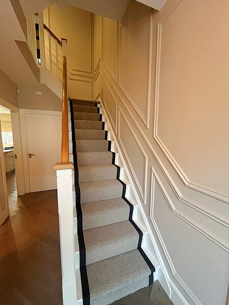 Front view and looking up of a white stairs and wood bannisters with full height wall of white stairs panelling and a wooden floor after being painted by Impressions Painting and Decorating