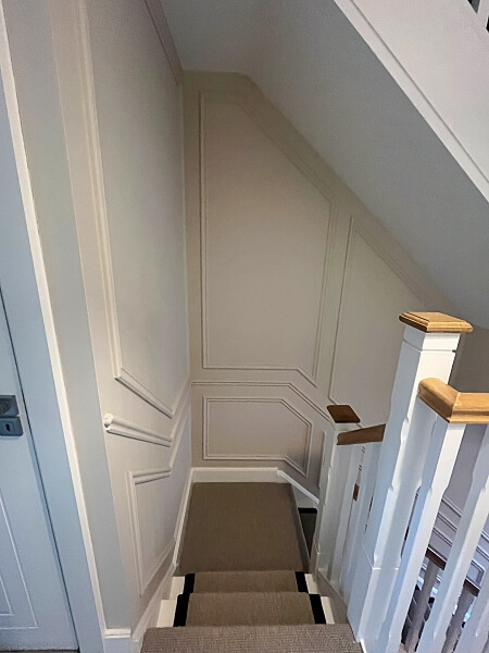 Looking down a staircase with a white stairs and wood bannisters on the right with full wall white stairs panelling on the left and front after being painted by Impressions Painters and Decorators