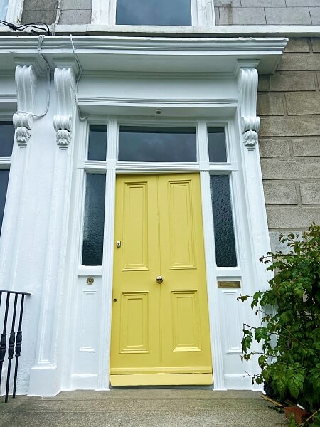 A freshly restored and painted yellow period door with glass panelling on the sides and top and a freshly painted white surround after being restored