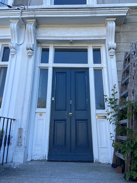 A navy blue period door with peeling paint and with glass panelling on the sides and top and a white surround with large sections of peeling paint before being restored