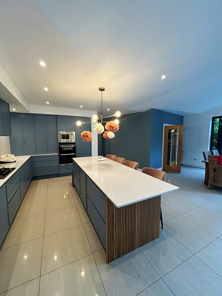 Kitchen island hand painted blue at an angle in the centre with hand painted blue kitchen cupboards at the back and the left hand side and blue wall in the right back ground with wooden door by Impressions painting and decorating Dublin