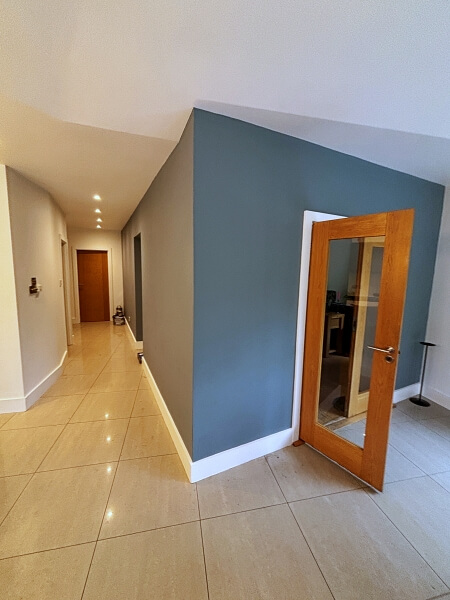 Corridor on the left to a brown door and blue wall on the right with a wooden door after being painted by Impressions house painting and decorating